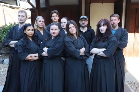 Group dressed in black martial arts robes posing with arms crossed outside dojo