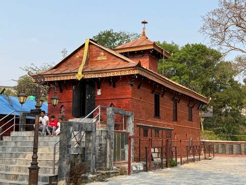 Small red-brick riverside temple with visitors sitting on the steps