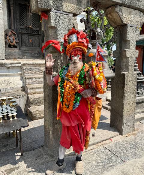 Brightly adorned sadhu with orange garlands raising his hand in blessing at Pashupatinath