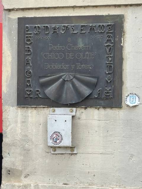 Plaque with Spanish text and sculpted fan design mounted on a stone wall.