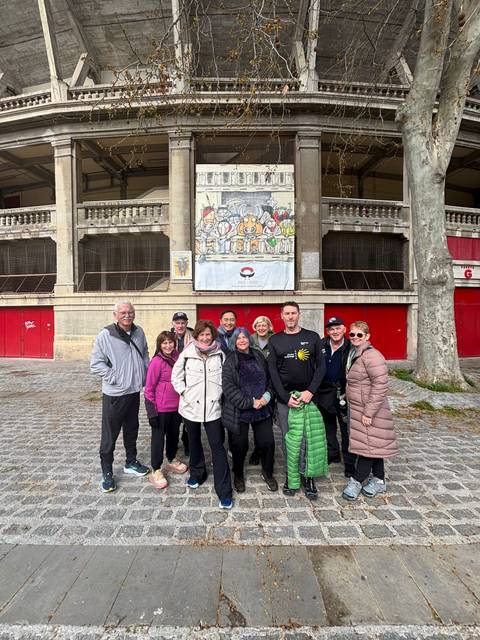 Smiling tour group posing in front of Pamplona bullring facade with cartoon banner.