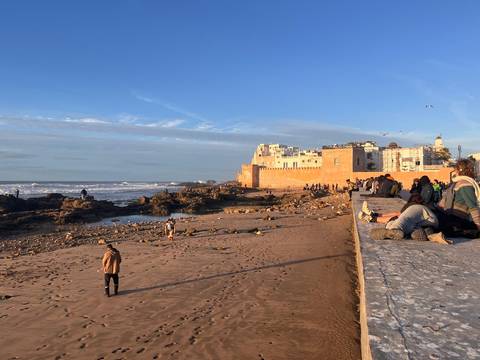 Relaxed beach scene outside Essaouira’s ochre ramparts with visitors lounging and strolling at sunset.