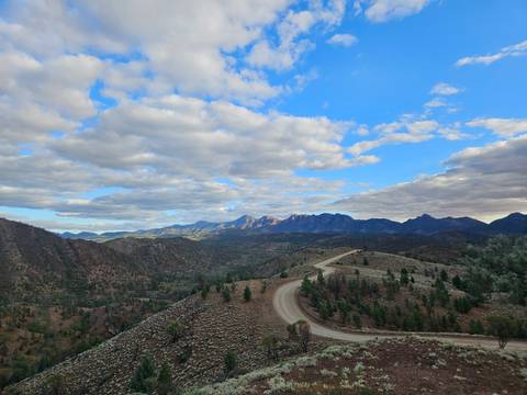 Wide view of a winding dirt road leading through rugged mountain ranges beneath a big sky filled with puffy clouds.