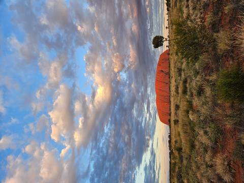 Iconic Uluru rises from the red desert plain beneath dramatic, pastel-lit evening clouds.