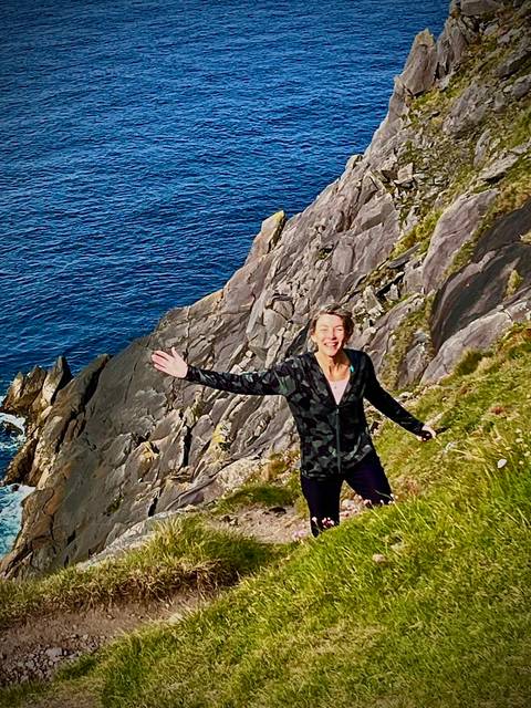 Smiling hiker poses on a green cliff edge high above the deep blue Atlantic Ocean.