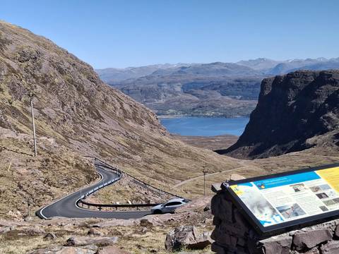Hair-pin Bealach na Bà road descending to a blue sea loch with information board in foreground