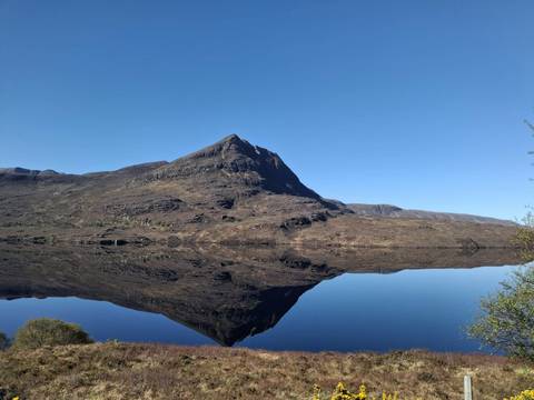 Cone-shaped mountain perfectly mirrored in an ultra-calm loch on a clear day