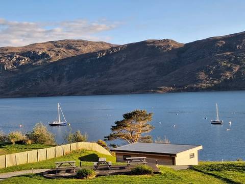 Peaceful coastal loch with anchored sailboats backed by rolling highland hills in evening light