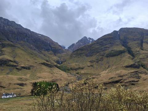 Cloudy view of a rugged Scottish mountain valley with a small waterfall trickling down rocky slopes covered in brown-green grass.