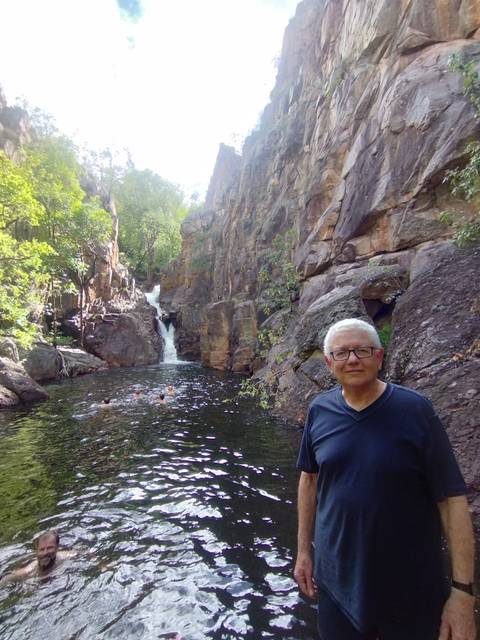 Visitor stands near a plunge pool and small waterfall while swimmers enjoy the water amid rugged cliffs