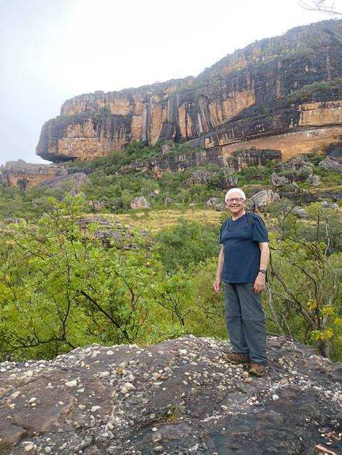 Hiker smiling in front of dramatic sandstone escarpments and lush bushland