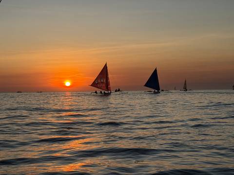 Colorful sailboats silhouetted against a fiery Boracay sunset on calm seas