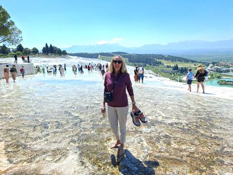 Visitor standing barefoot on the white travertine terraces of Pamukkale with distant mountains and other tourists behind her