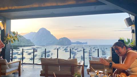Open-air lounge overlooking El Nido bay filled with boats and dramatic limestone cliffs at dusk.