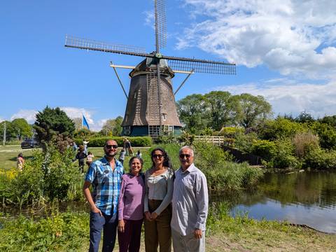 Group of travellers stands in front of a classic Dutch windmill reflected in a pond on a sunny day.
