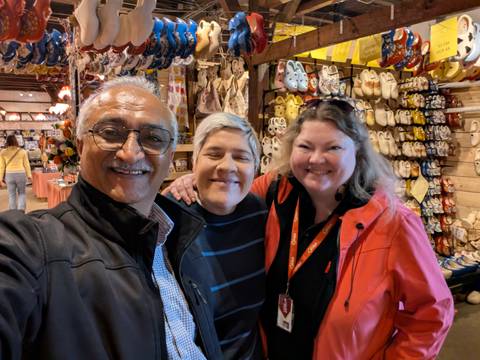 Three travellers smile inside a souvenir shop displaying rows of traditional wooden clogs and other goods.