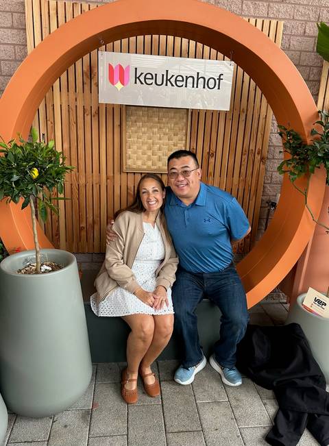 Smiling couple seated on a stylish bench with wooden slat backdrop and potted plants.
