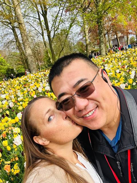 Close-up selfie of a couple with vibrant yellow and white tulip field in bloom behind them.