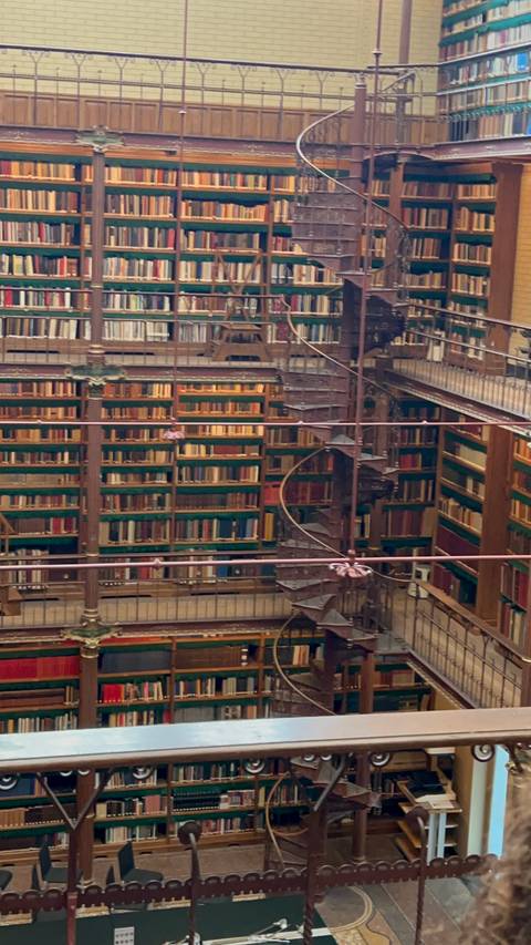 Interior view of a grand multi-level library with wrought-iron spiral staircase and shelves full of books.