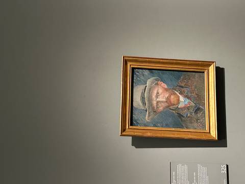 Framed self-portrait painting by Vincent van Gogh displayed on a grey museum wall.