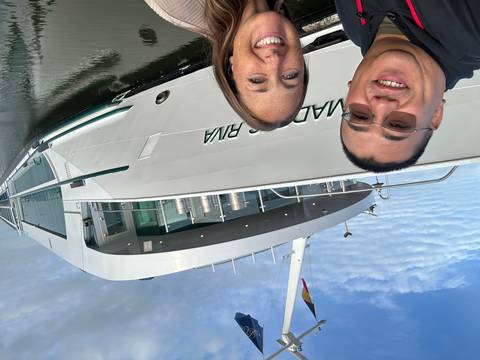 Couple taking a selfie in front of the modern white river cruise ship 'Amadeus Riva' docked on a calm waterway.