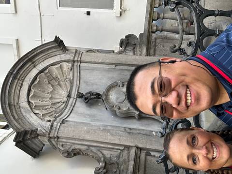 Selfie of travellers smiling in front of the famous Manneken Pis fountain in Brussels.