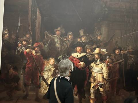 Older visitor admiring Rembrandt’s famous ‘Night Watch’ painting in a museum gallery.