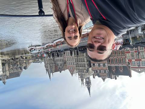 Couple posing on a bridge with historic stepped-gabled buildings, boats and canal of Ghent behind them.