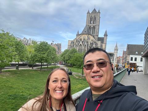 Couple posing on a bridge with a gothic church and green park area in the background.