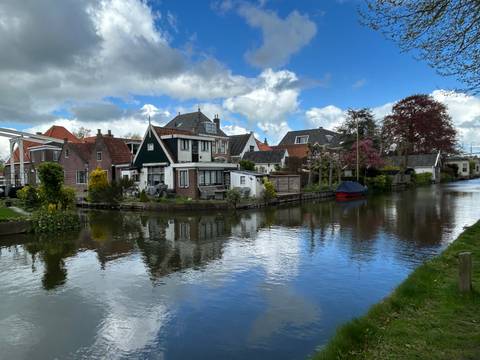 Quaint Dutch canal lined with traditional brick houses reflected in calm water beneath a mixed sky.