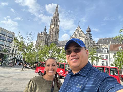 Couple smiling with the spired Cathedral of Our Lady towering above a sunny city square.