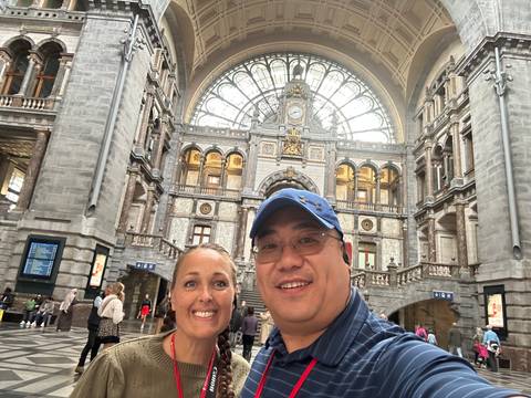 Selfie of a couple inside an ornate railway station hall with grand arches and a glass dome.