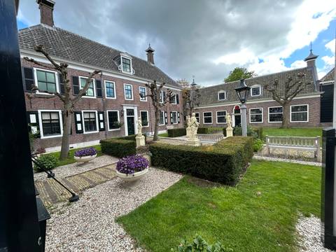 Trimmed gardens with statues and brick manor houses under a partly cloudy sky.