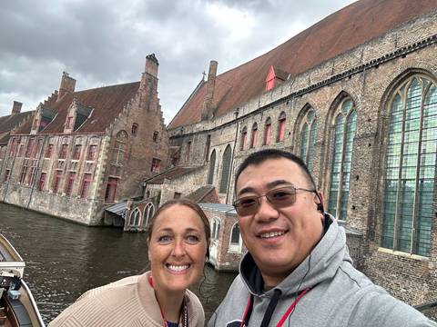 Couple posing beside a medieval brick hospital complex along a canal in overcast weather.