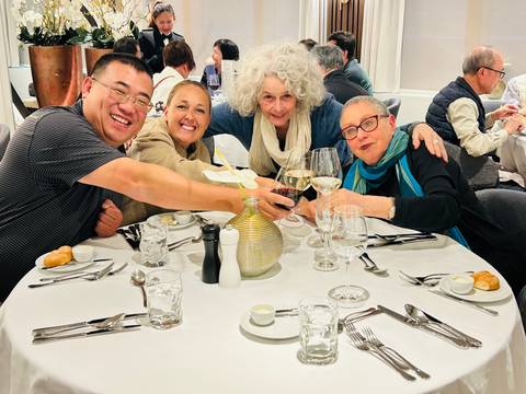 Friends toasting with wine around a white-clothed dining table in a bright restaurant.