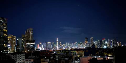 Nighttime skyline of Manila with illuminated skyscrapers against a dark blue sky.