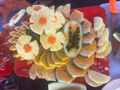 Festive tropical fruit platter decorated with carved pineapple flowers and 'Port Barton' lettering.