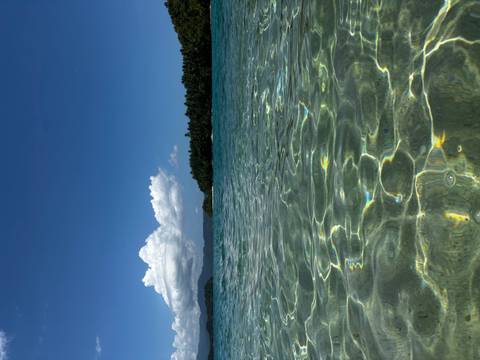 Crystal-clear shallow sea water with distant wooded island under blue sky and clouds.