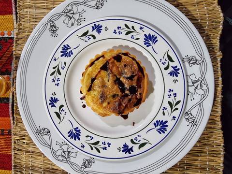 Close-up of small Moroccan-style savory tart drizzled with dark sauce on decorated ceramic plate.