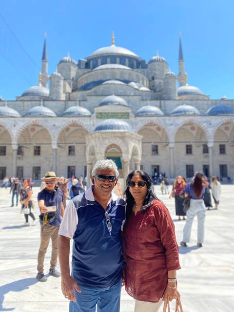 Smiling couple in courtyard of historic mosque with domes and arches under bright sun