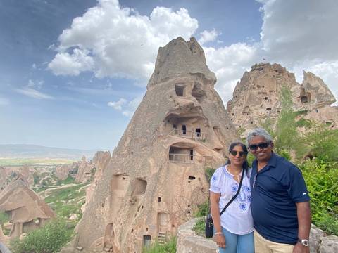 Visitors standing before towering honey-coloured rock cone dwellings with cave windows, under partly cloudy sky