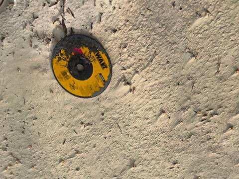 A damaged circular saw disc lying partially buried in light sand