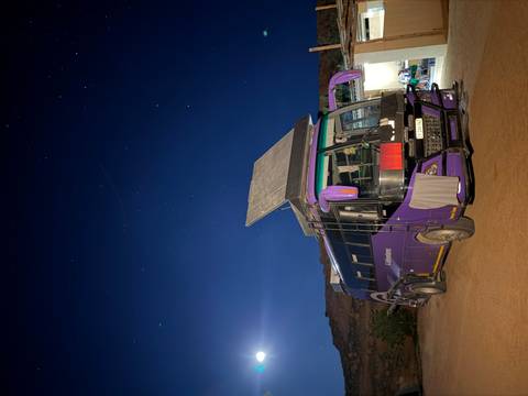 Purple overland adventure truck parked under a starry sky with solar panels raised.