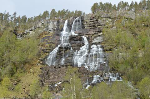 Multi-tiered waterfall cascades down a wooded cliff in the Norwegian fjords during spring