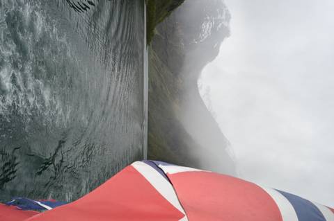 Foggy fjord scene seen from the stern of a boat with Union Jack flag and misty mountains ahead