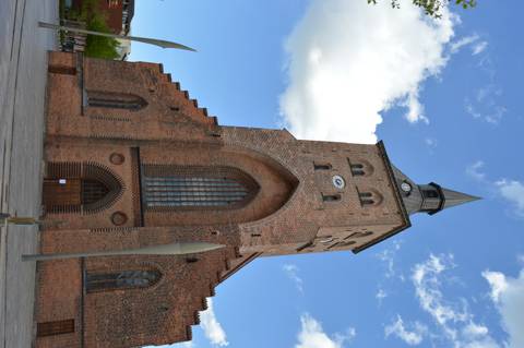 Tall red-brick Gothic church with pointed spire and blue sky in a Danish city square