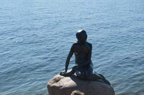 Bronze Little Mermaid statue sits on a rock gazing over the Copenhagen harbour waters