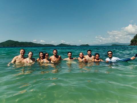 Group of smiling travelers waist-deep in clear tropical sea with green islands on the horizon.