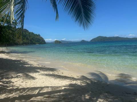 Pristine tropical beach with white sand, clear blue water and distant green islands under a sunny sky.