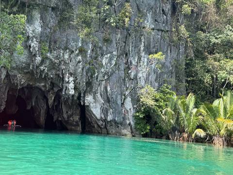 Turquoise river flowing from a dramatic limestone cave entrance fringed by palms in the jungle.
